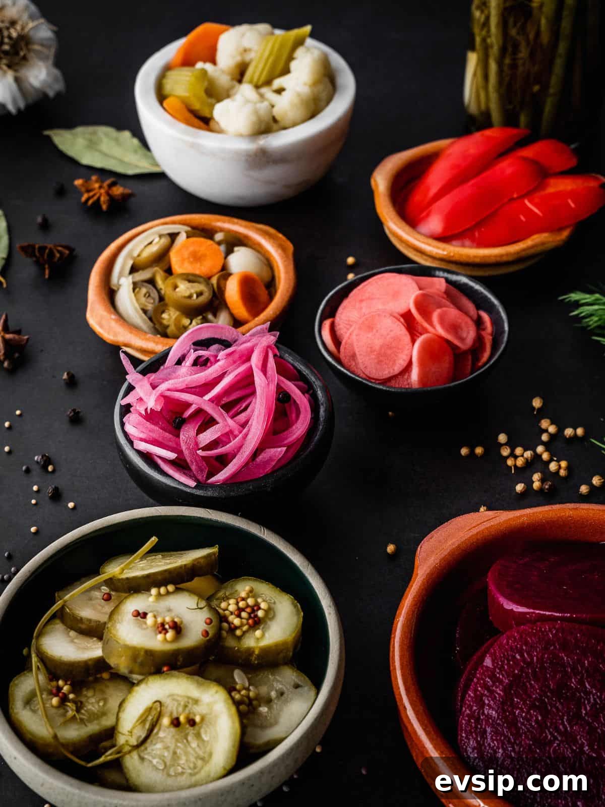 A spread of small bowls with pickled cucumbers, beets, onions, radish, peppers, and cauliflower. 