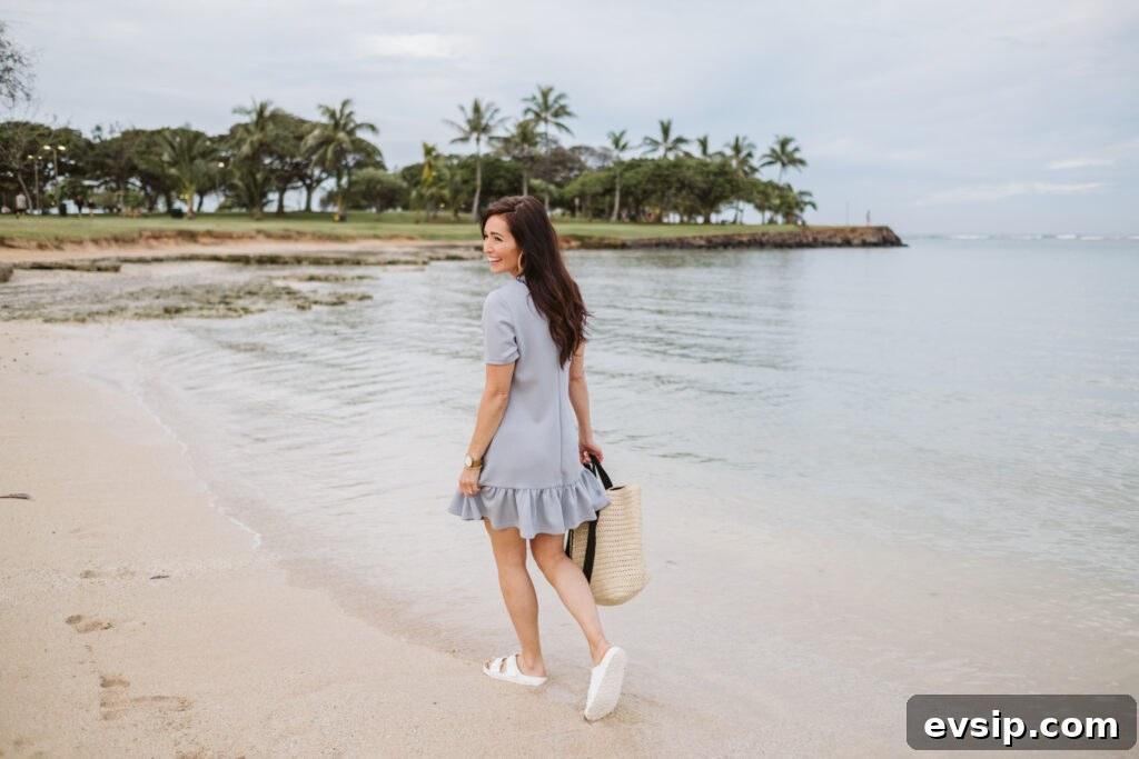 Tori on the beach in Hawaii walking with sandals in the water in a blue tee shirt dress from The Fraîche x PRIV Summer Collection