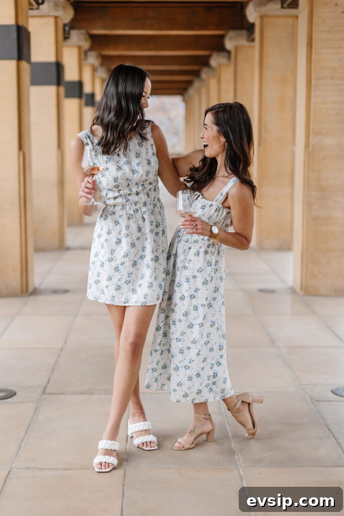 Two women smiling and laughing at a winery in summer dresses with glasses of wine.