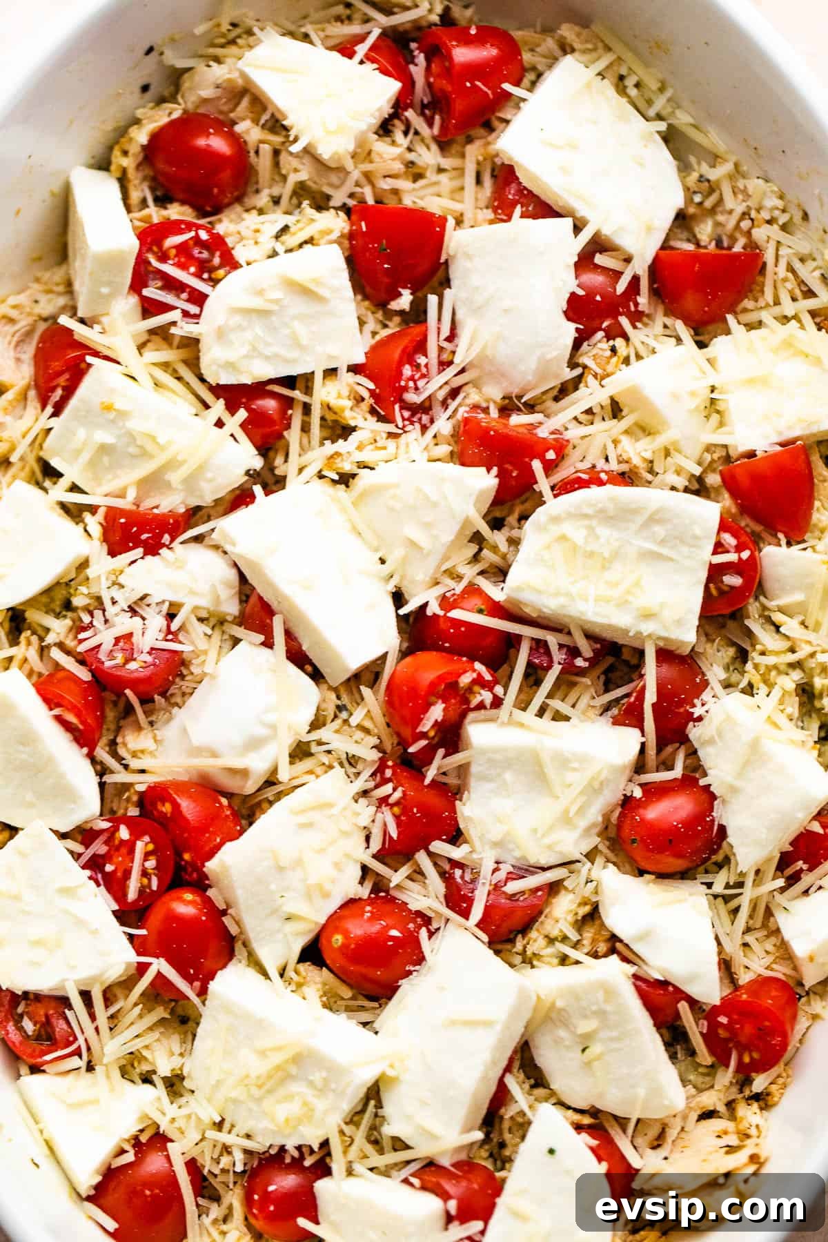 chicken caprese casserole in a white baking dish topped with fresh mozzarella chunks and cherry tomatoes