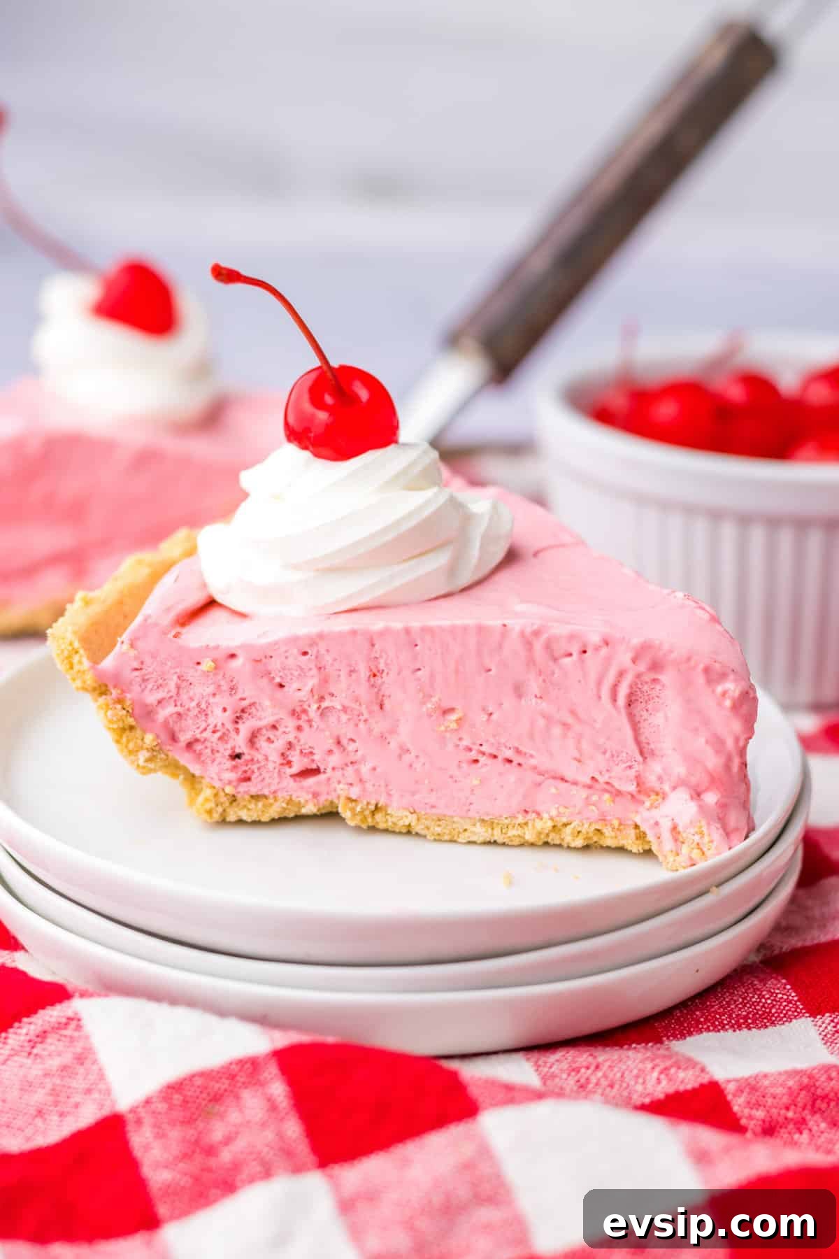 Slice of no bake kool aid pie with cool whip and cherry on top.
