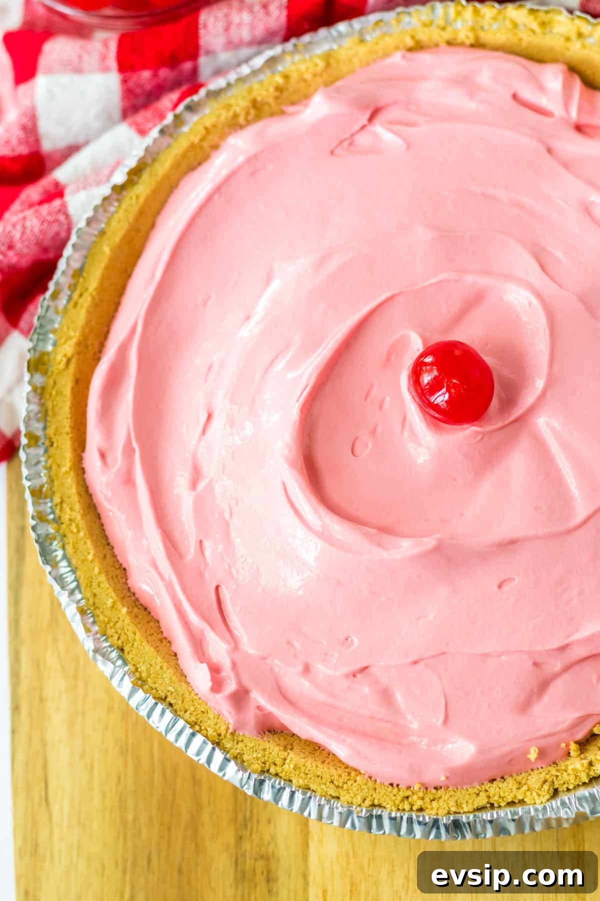 Overhead photo of pink, creamy no bake kool aid pie in graham cracker crust with maraschino cherry in the center.