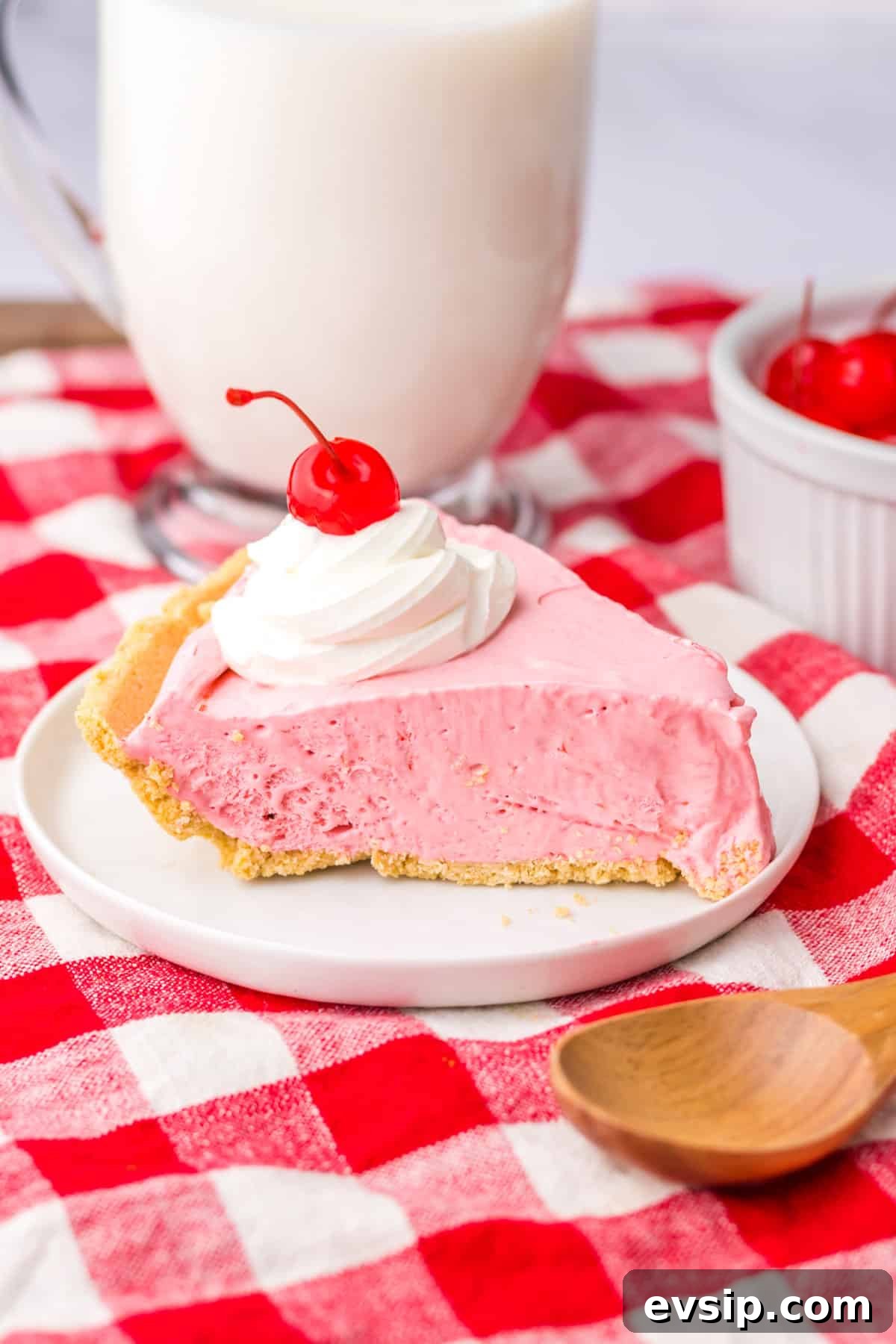 Slice of cherry cool aid pie on white plate with large glass of milk in the background.