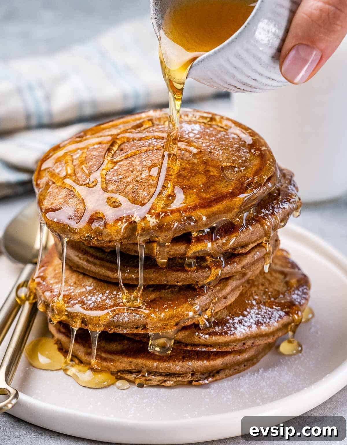 Drizzling honey over a stack of gingerbread pancakes on a white plate.