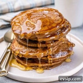 side shot of stacks of pancakes on a white plate with honey drizzled over