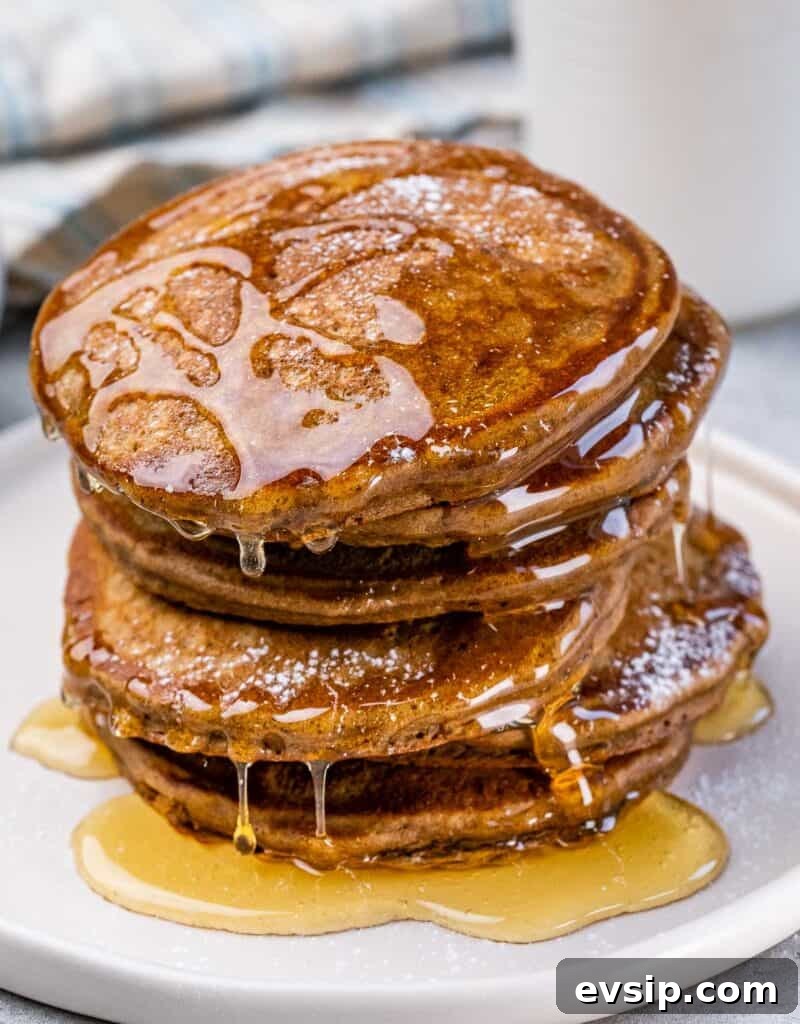 side shot of stacks of pancakes on a white plate with honey drizzled over it