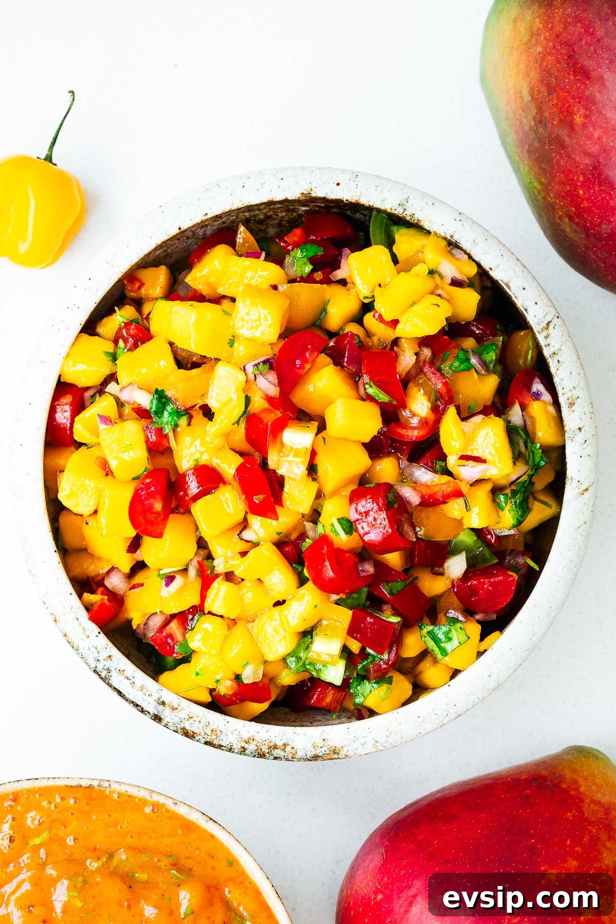 Mango Habanero Salsa Recipe — Fresh Homemade Fruit & Chili Salsa 2 A bowl with fresh mango habanero salsa alongside a bowl of roasted mango habanero salsa surrounded by fresh mangoes and habanero peppers.
