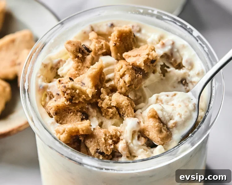 Vanilla protein ice cream topped with cookie dough with spoon digging up the top.