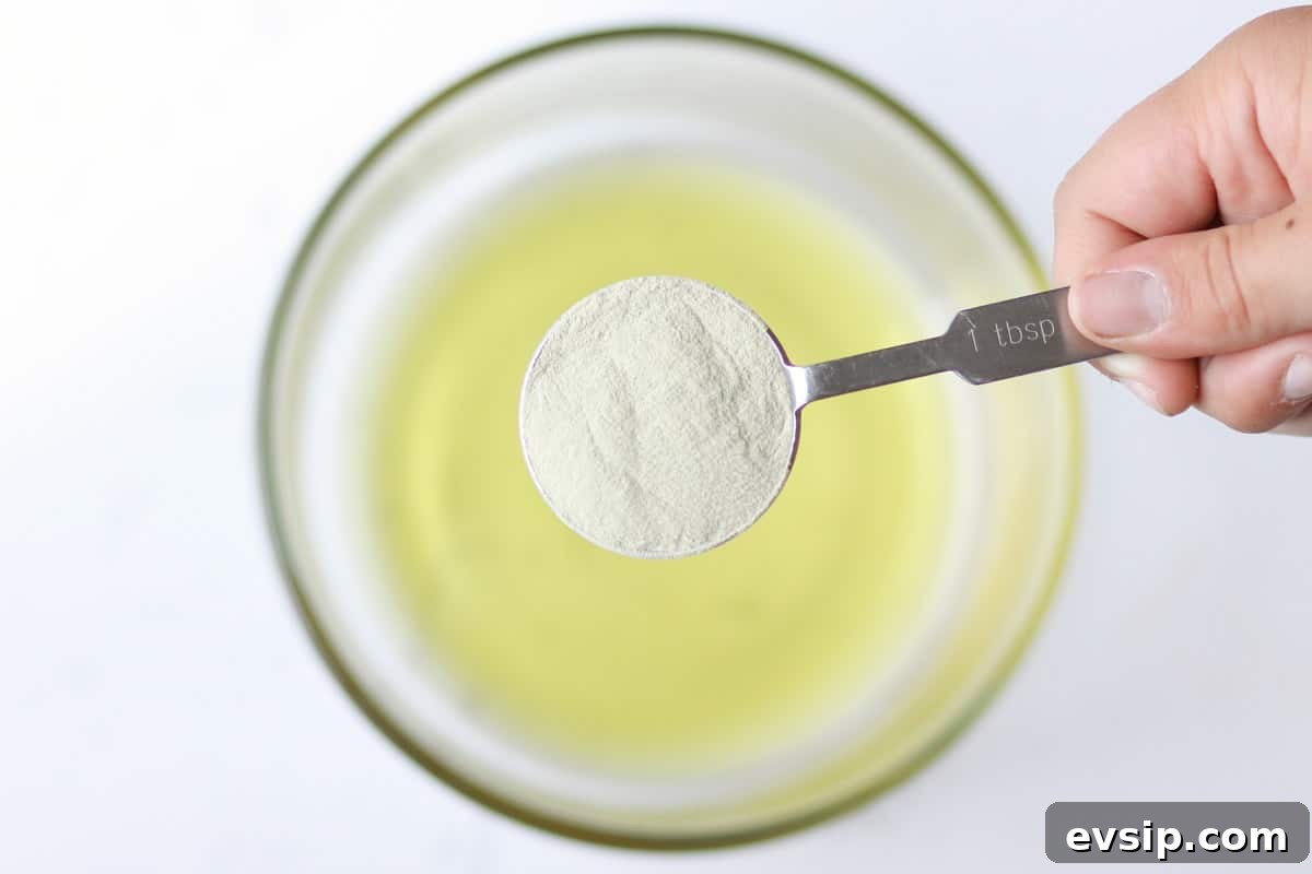 a tablespoon of bentonite clay being added to a bowl of melted oils to make anti-itch cream
