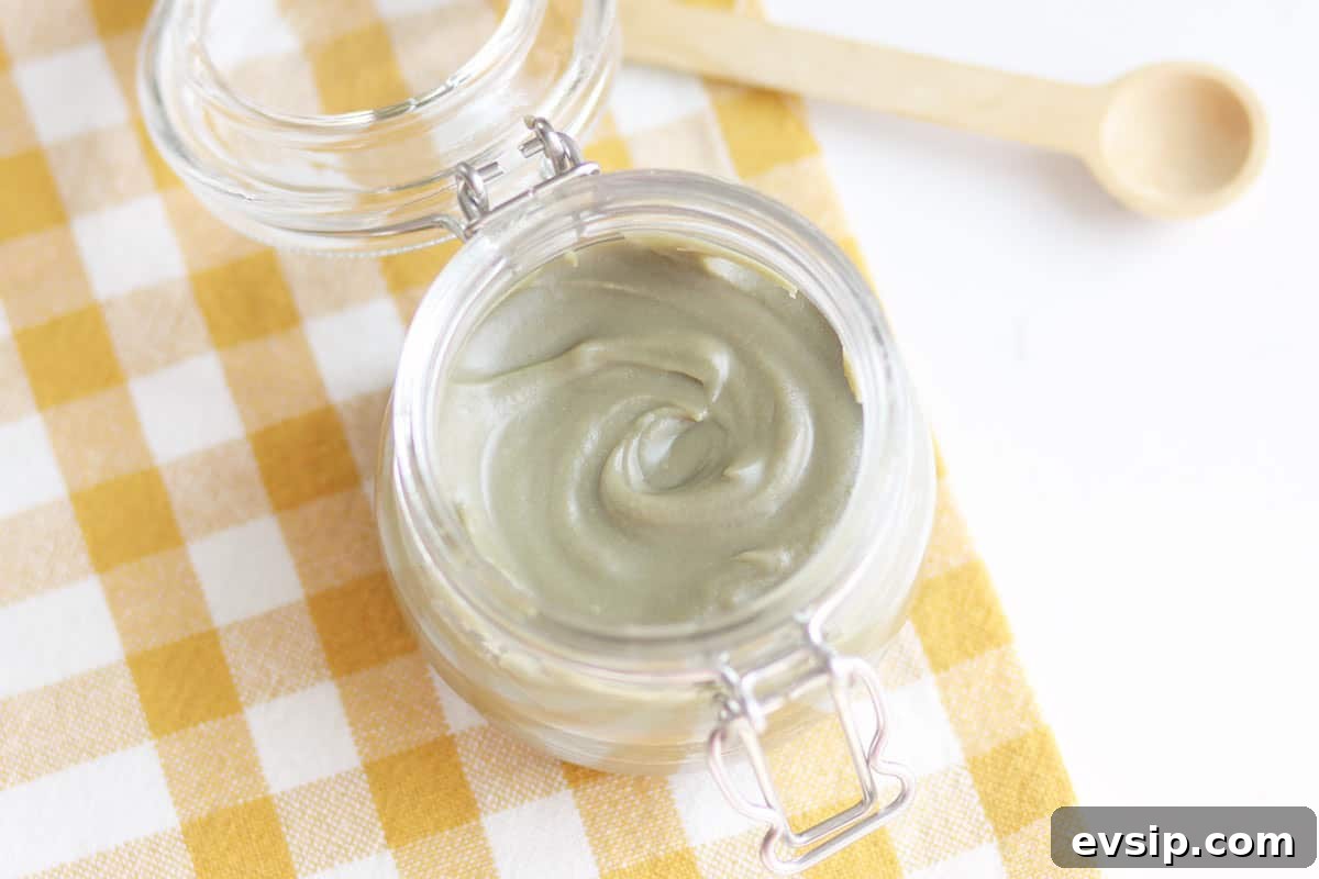 a jar of homemade anti-itch cream on a checkered yellow towel with a wooden spoon next to it