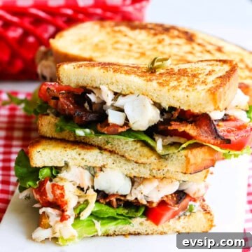 A sliced open BLT sandwich loaded with succulent lobster, bacon, lettuce and tomato stacked on a board.