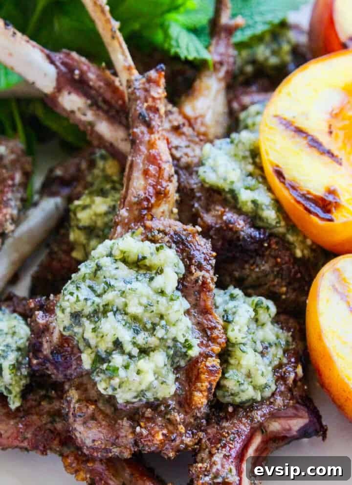 A white platter filled with grilled lamb chops topped with mint pesto and grilled peaches.