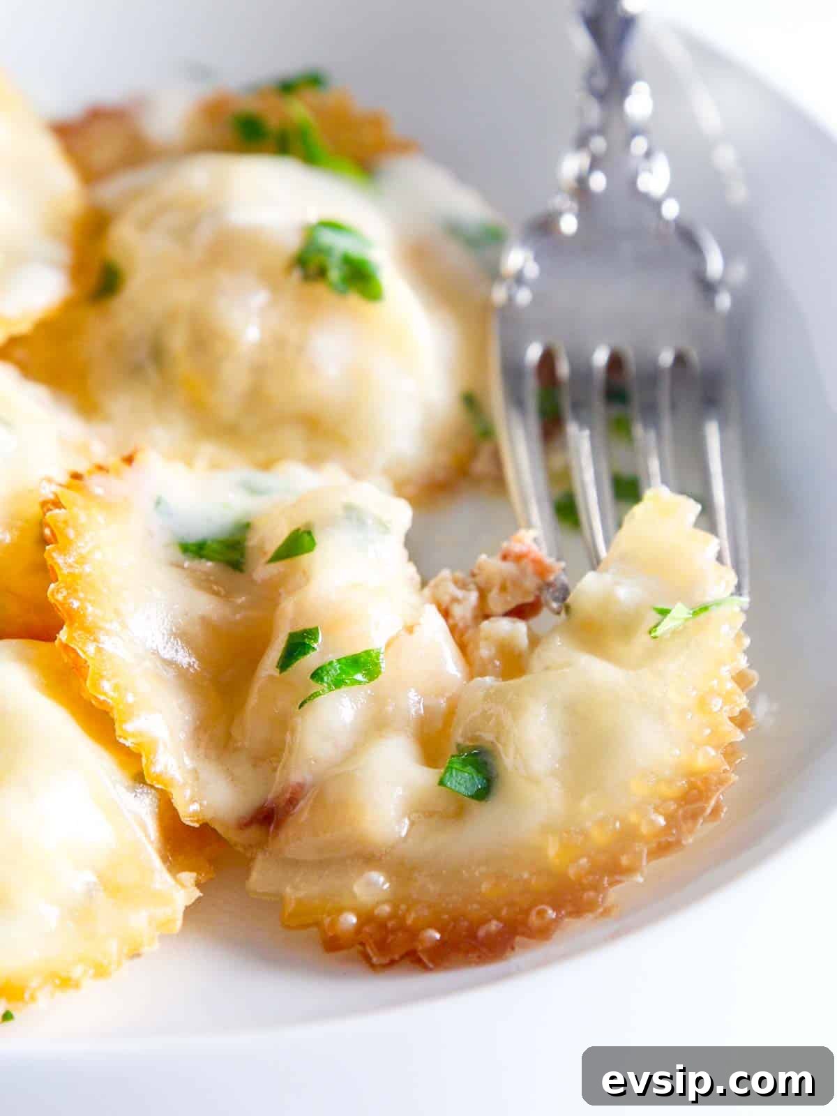 A silver fork cutting into a lobster ravioli on a white china plate.