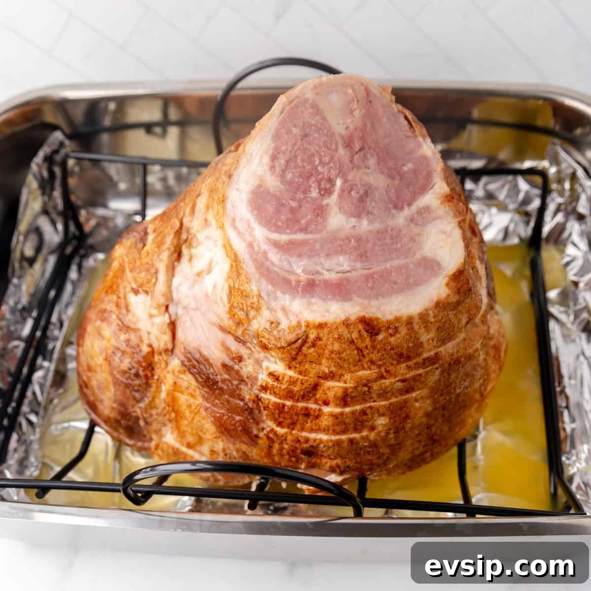 A cooked ham placed on a rack inside a foil-lined roasting pan.