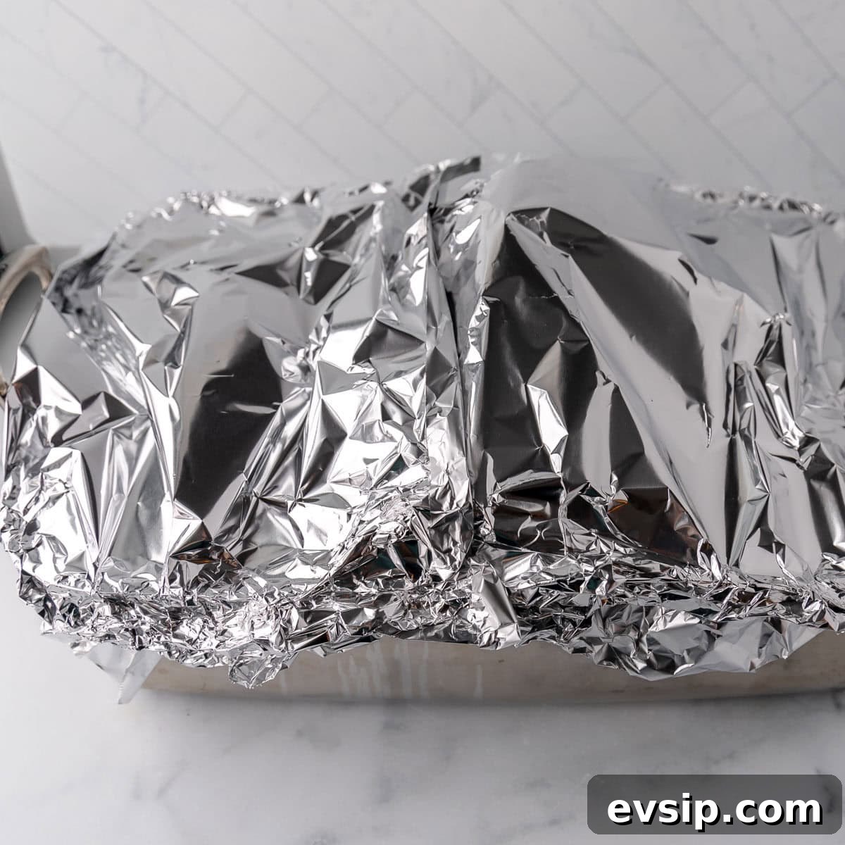 A dish covered with crumpled aluminum foil on a marble surface.