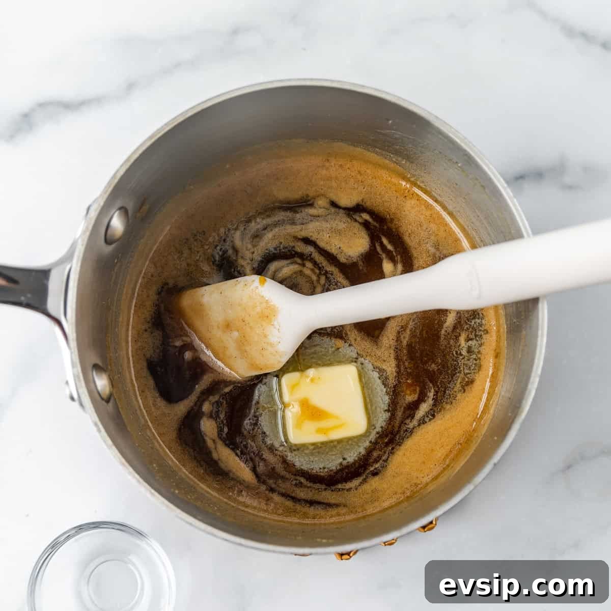 Butter melting and browning in a saucepan with a spatula on a marble surface.
