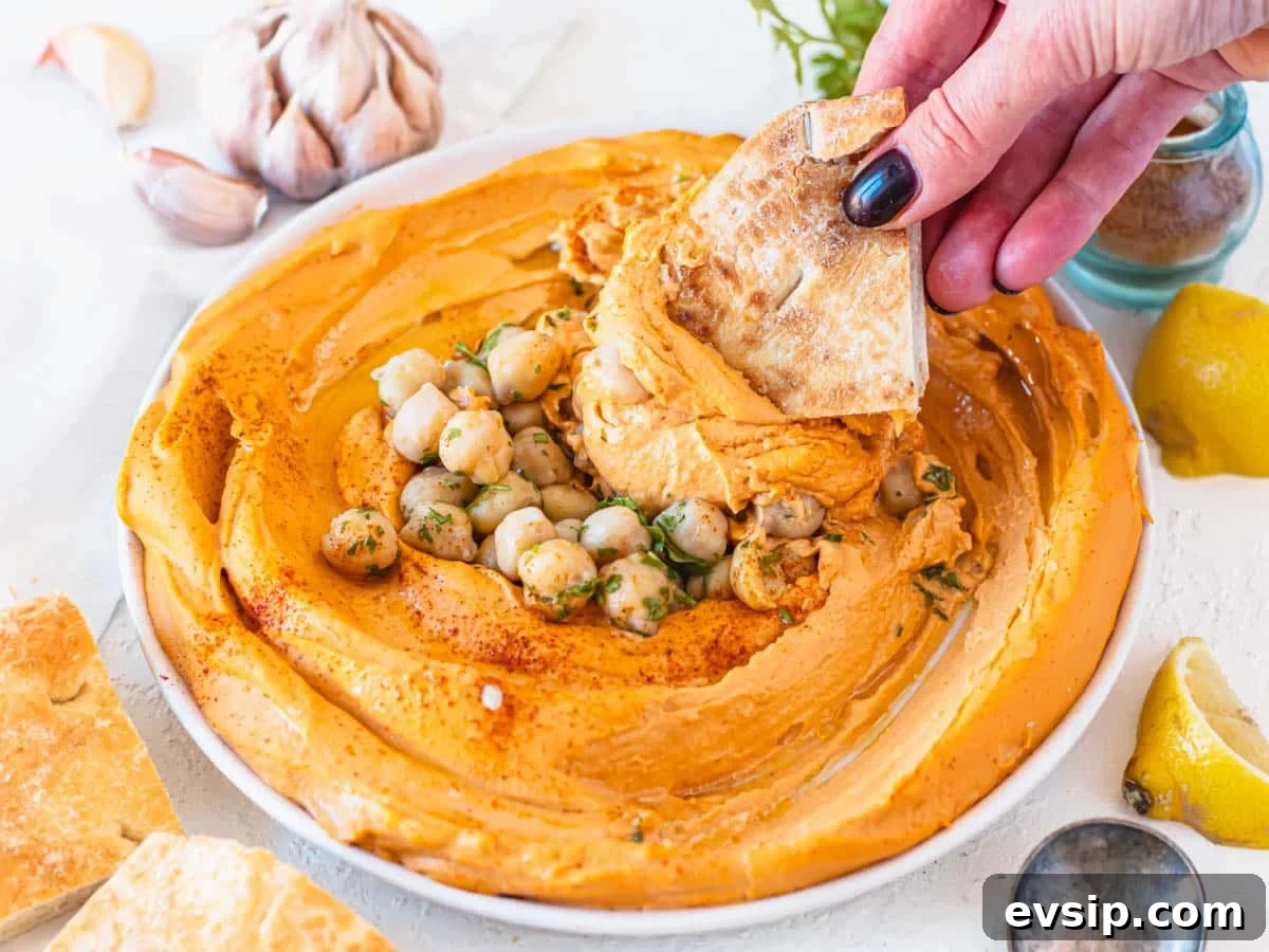 roasted pepper hummus in a white bowl with hand holding a pita bread
