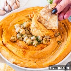 roasted red pepper hummus with chickpeas and hand holding a pita chip