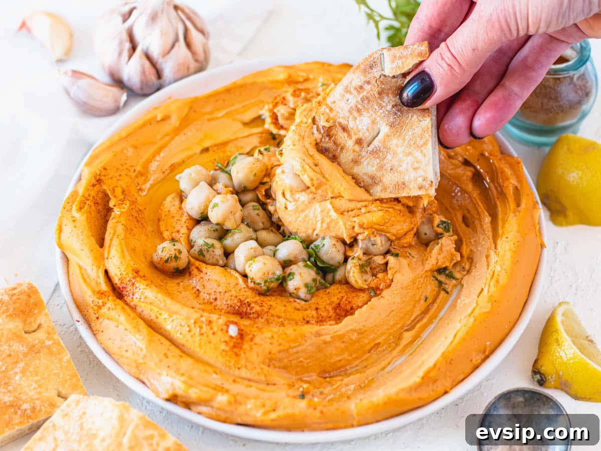 roasted pepper hummus in a white bowl with hand holding a pita bread