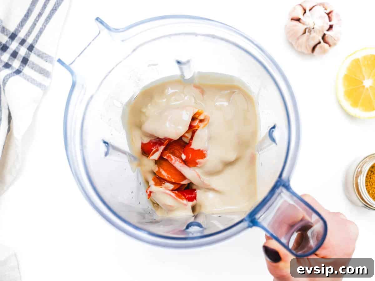 tahini and red bell pepper in a blender held by a hand
