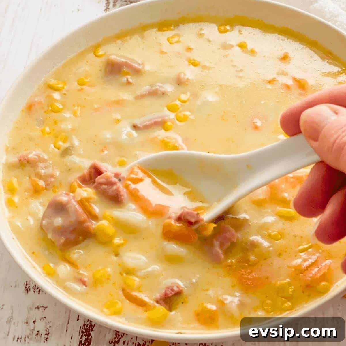 A bowl of pressure cooker ham and potato soup with a white spoon dishing up some soup.