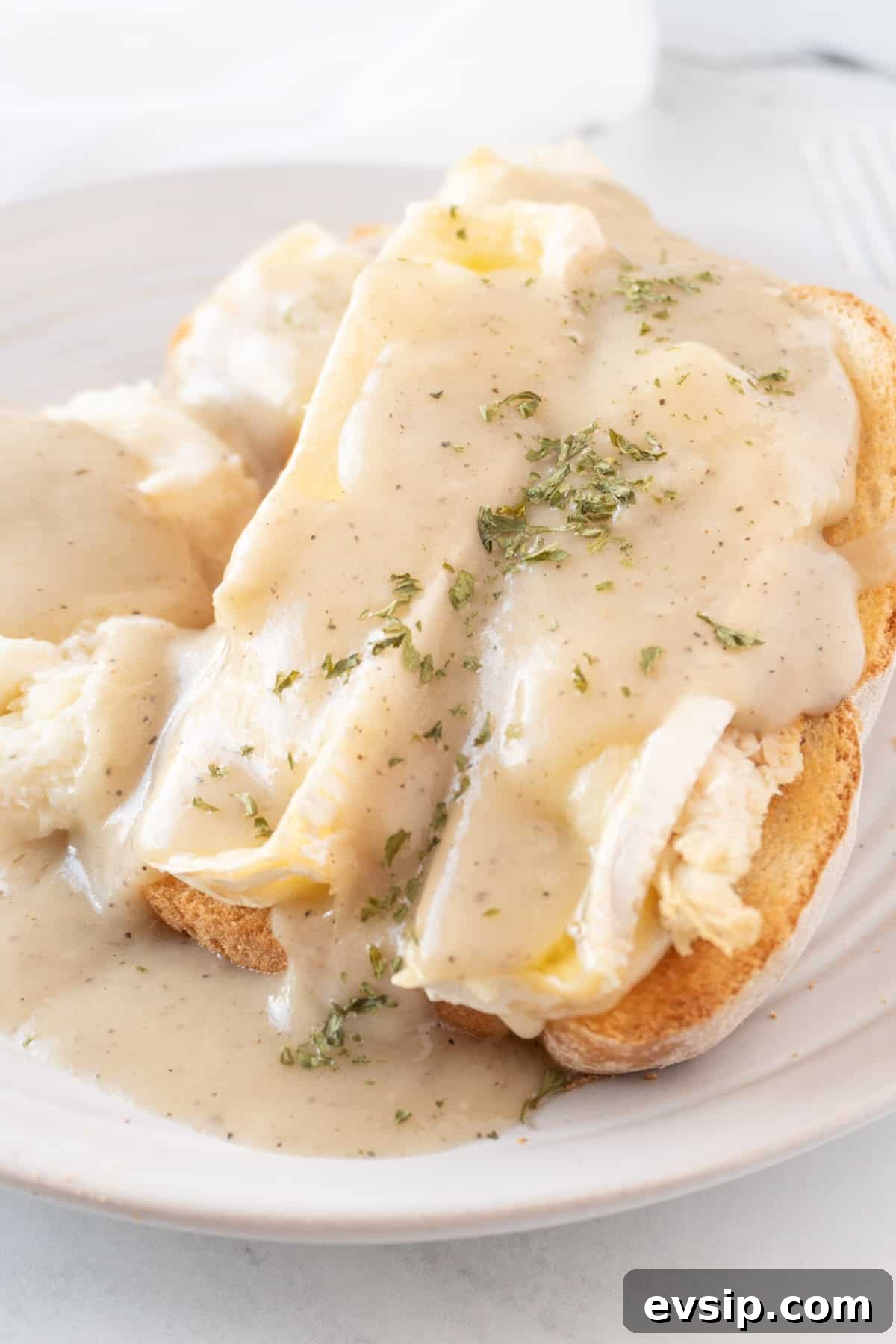 Open-faced hot turkey sandwich with brie and gravy on a white plate next to mashed potatoes.