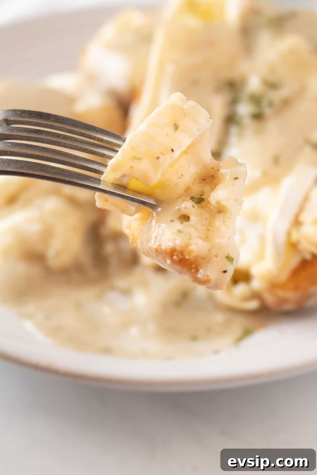 A piece of a hot turkey sandwich with gravy on a fork, with the sandwich in the background.