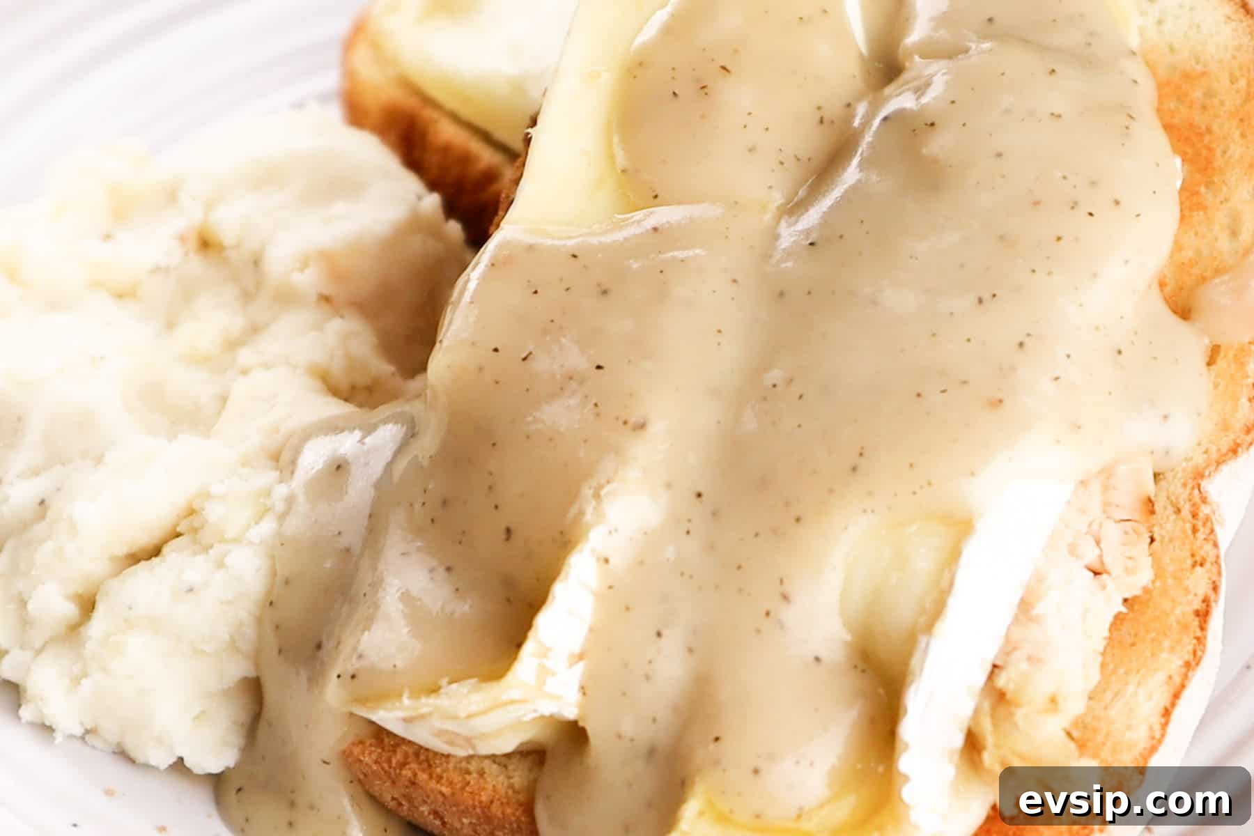 Gravy is added on top of the hot turkey sandwich. The sandwich is on a white plate next to mashed potatoes.