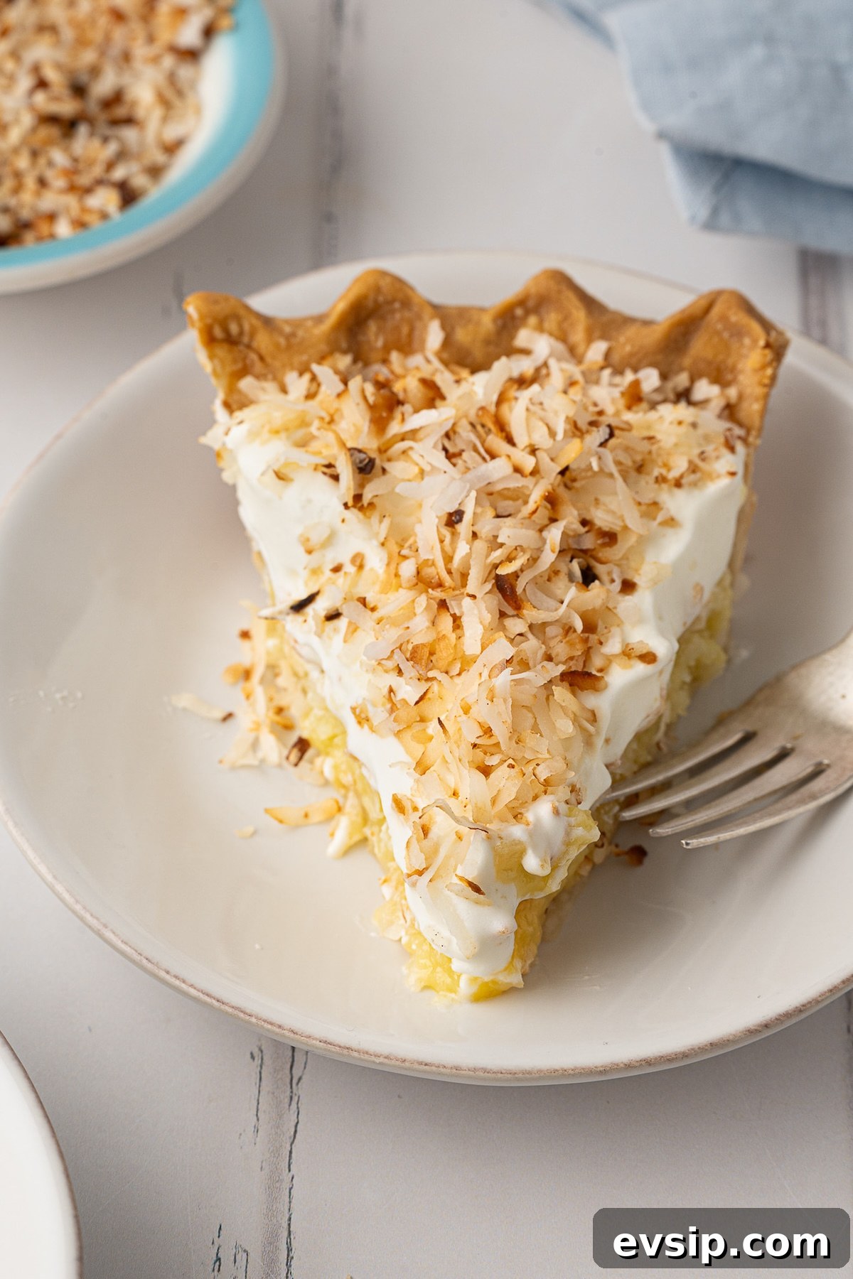 A close-up of a slice of easy coconut pie, focusing on the contrast between the dense, baked custard-like pie filling and the light, powdered sugar sweetened whipped topping