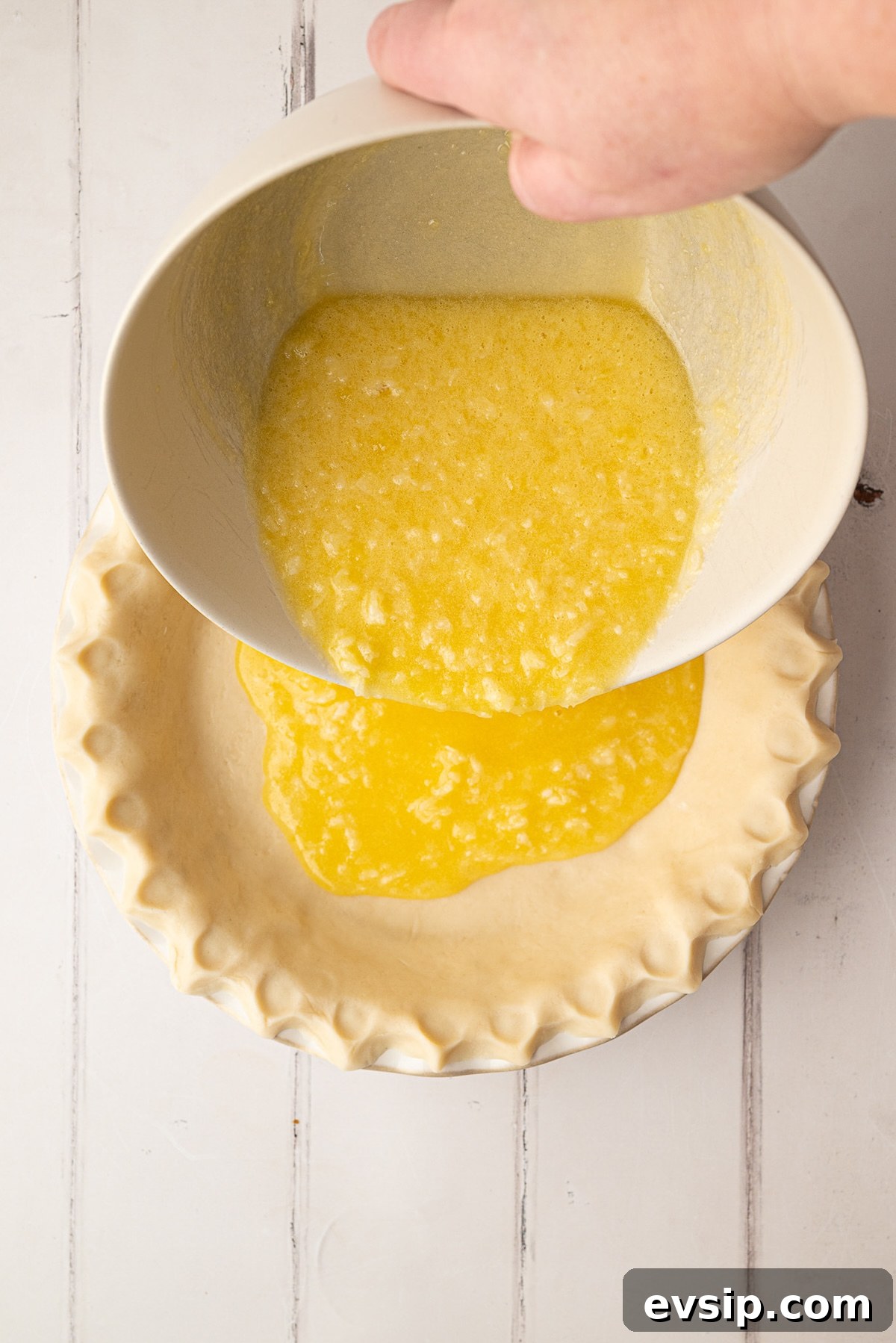 Pouring a smooth, whisked buttermilk and coconut pie filling directly into an unbaked pie crust before baking.