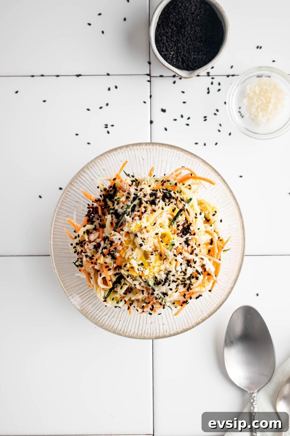 Kani salad in a glass bowl on a white tile counter. Beind it is a white cup of black sesame seeds.