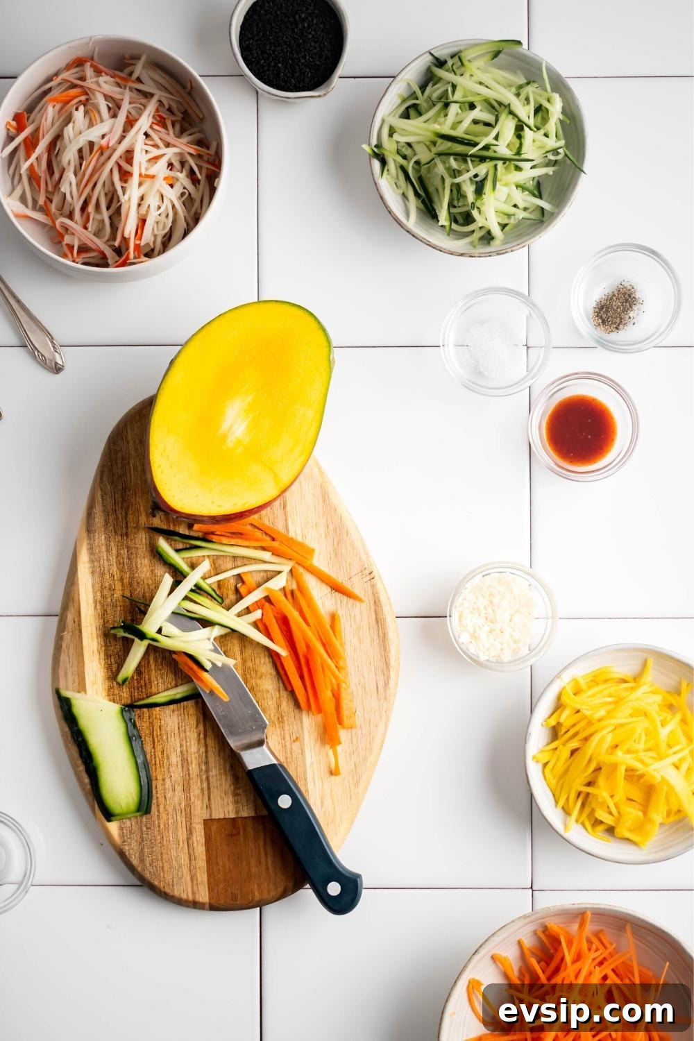 Julienned cucumber, carrot, mango and bowls of ingredients on a counter.