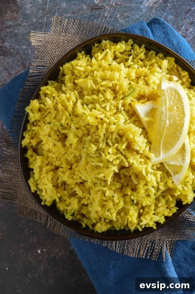 An overhead view of a dark bowl with yellow rice and 2 half slices of lemon on top