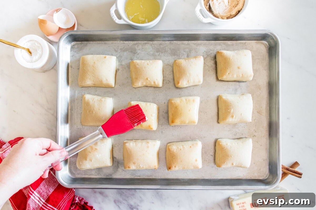 brushing texas roadhouse rolls with melted butter on a baking sheet