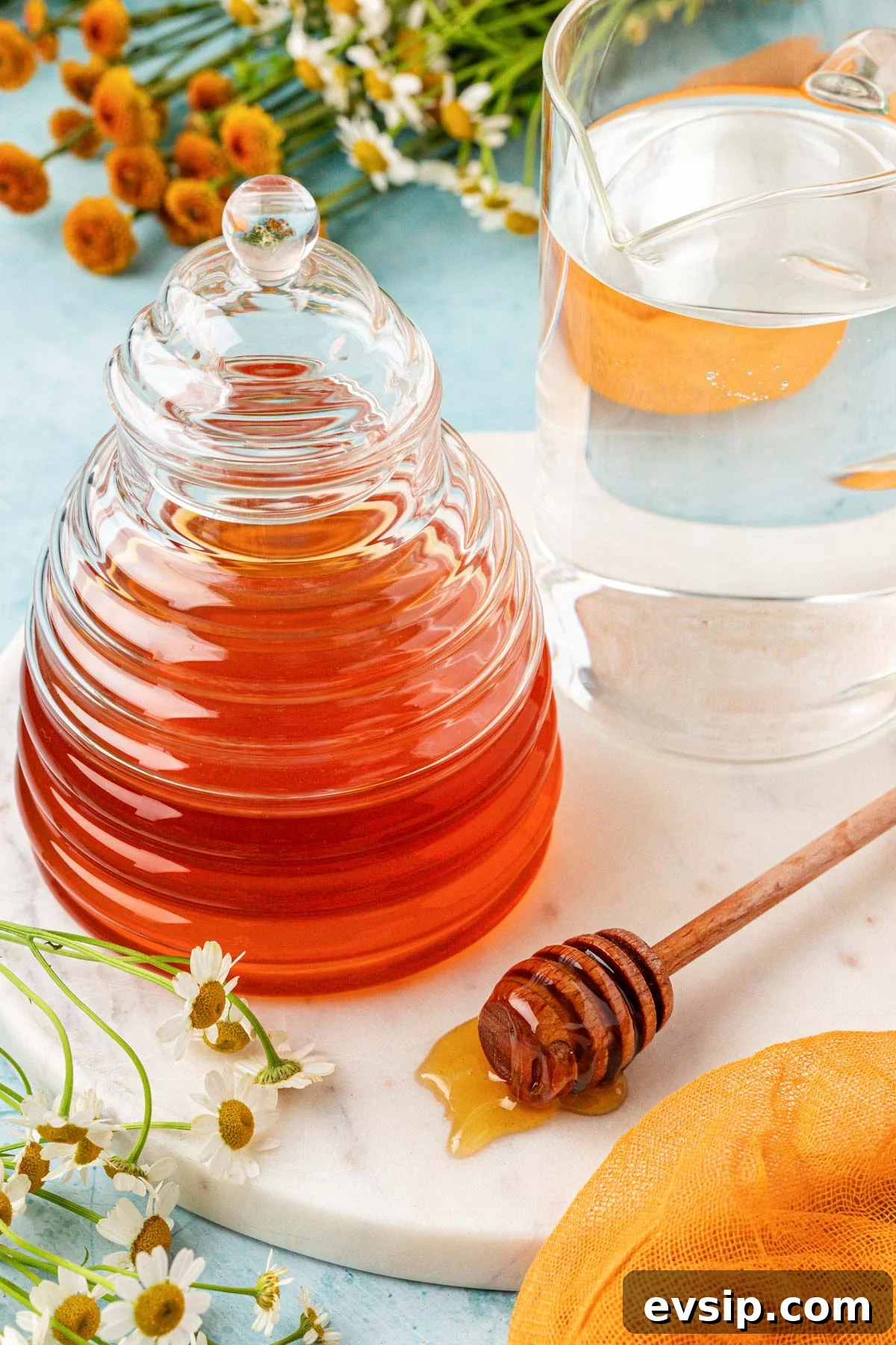 A glass of water and a glass container of honey on a table.