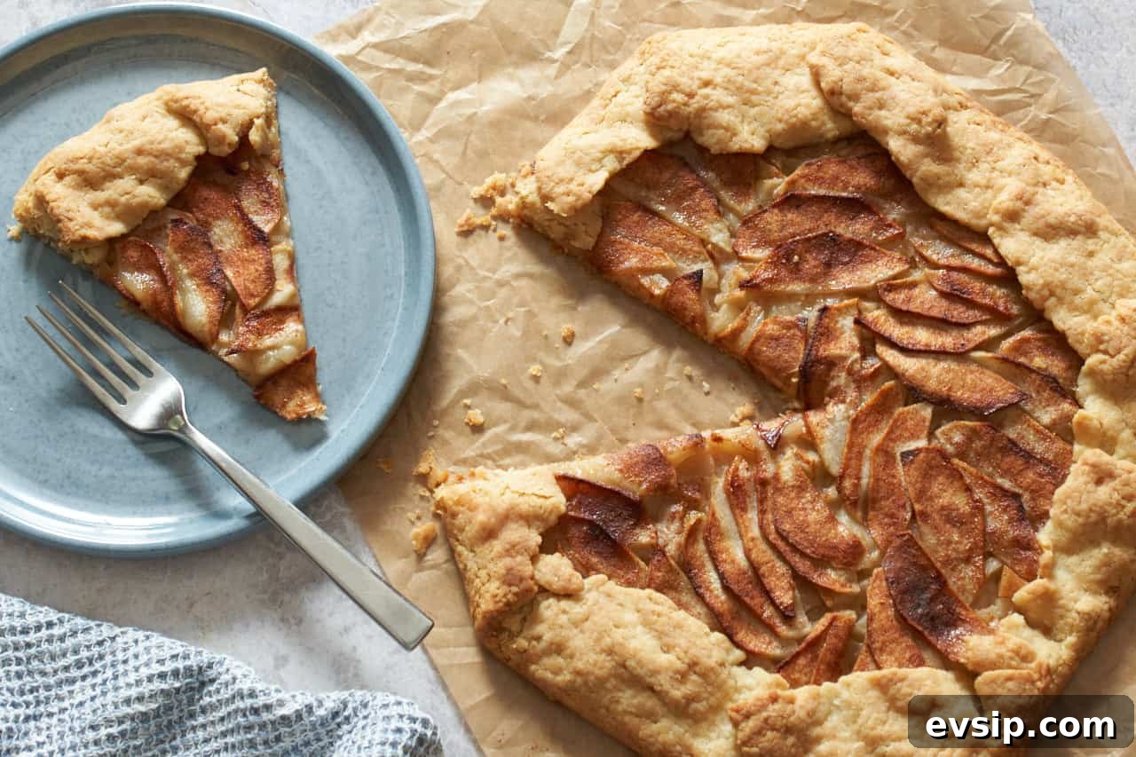 An apple galette with a slice cut out of it on a piece of parchment paper. A blue plate with a slice of galette and a blue napkin are on the left.