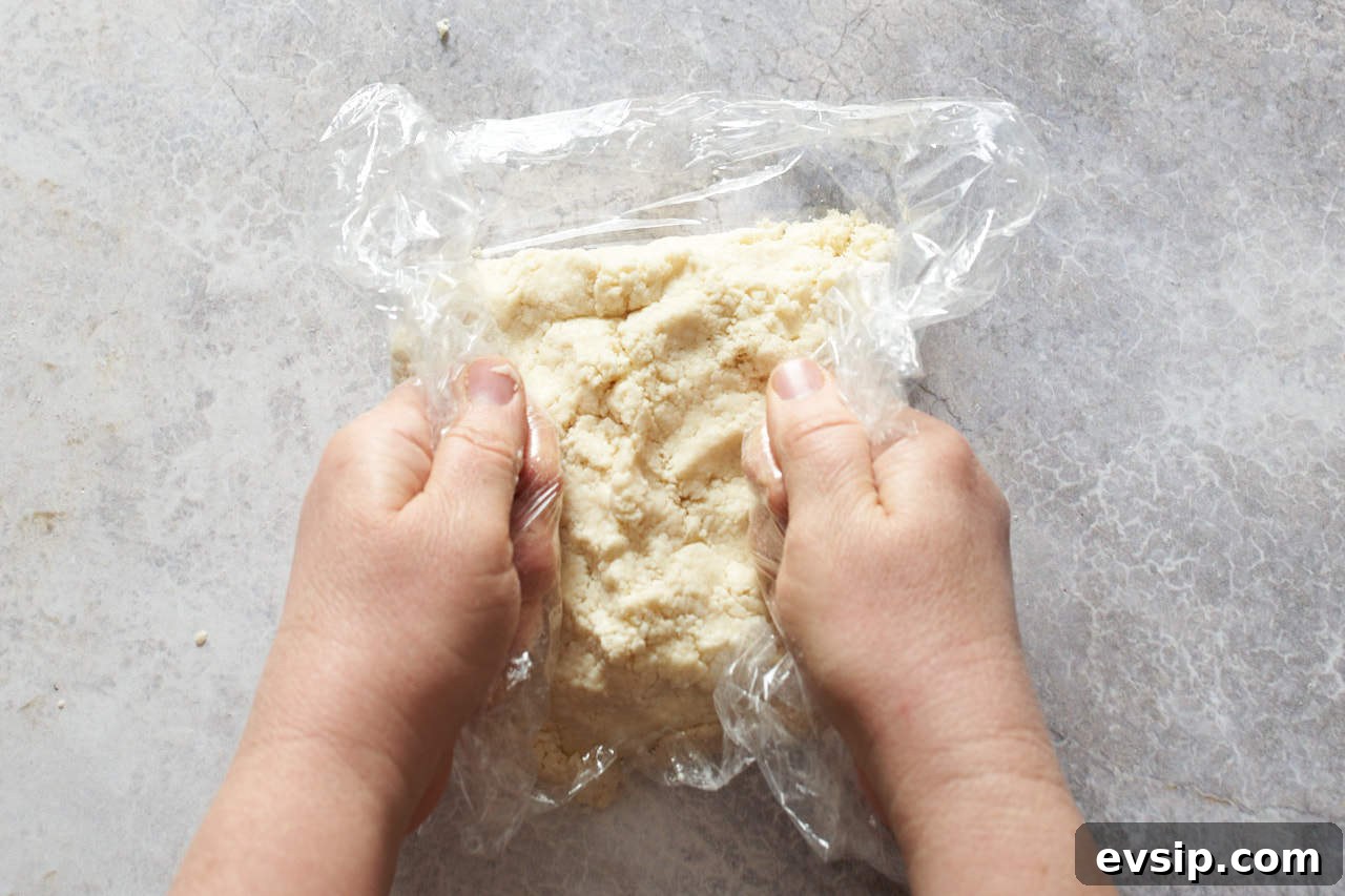 A woman's hands compressing galette crust into a disc in a piece of plastic wrap.