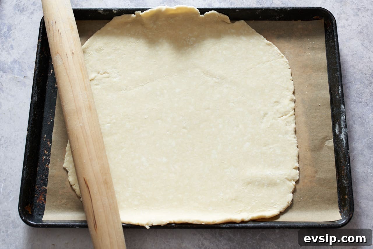 Galette crust rolled out and placed on a sheet pan lined with parchment paper. A rolling pin is on the left.