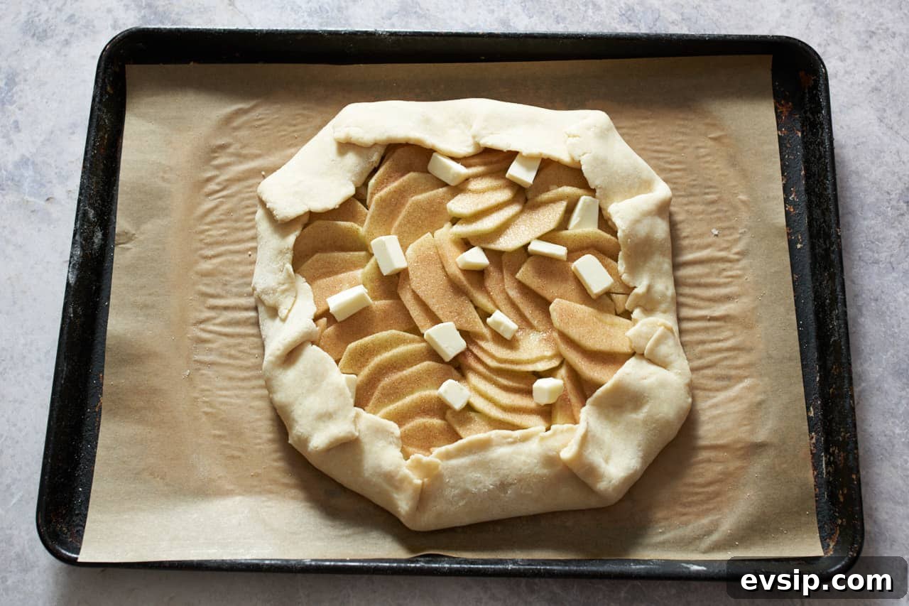 An apple galette with small pieces of butter on top ready to go into the oven.