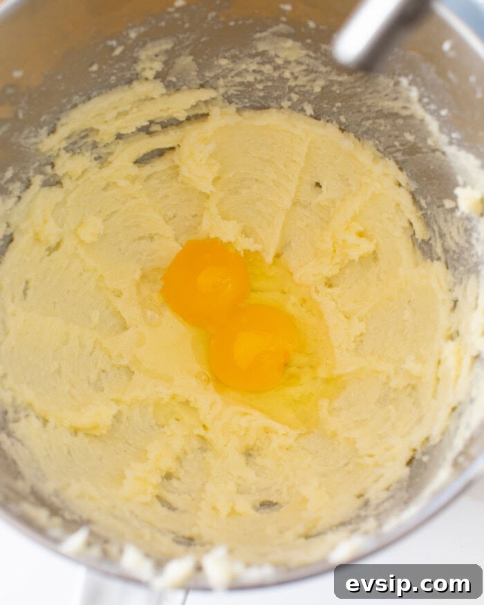 Butter and sugar mixture mixed with two raw eggs on top in a stand mixer bowl.