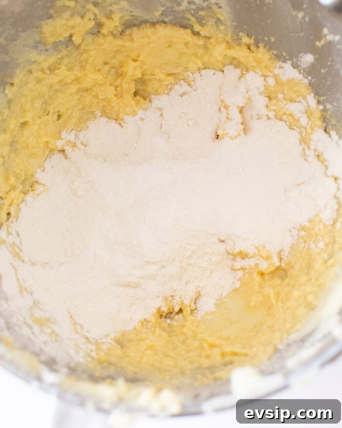 Butter, sugar, and egg mixture with flour on top in a stand mixer bowl.