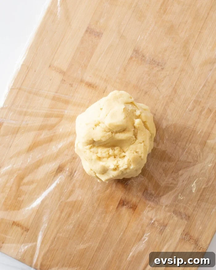 Sugar cookie dough rolled into a ball on top of plastic wrap on a cutting board.