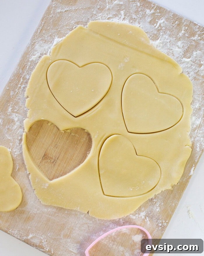 Sugar cookie dough rolled out into a thin layer on a wooden cutting board with heart shaped cutouts.