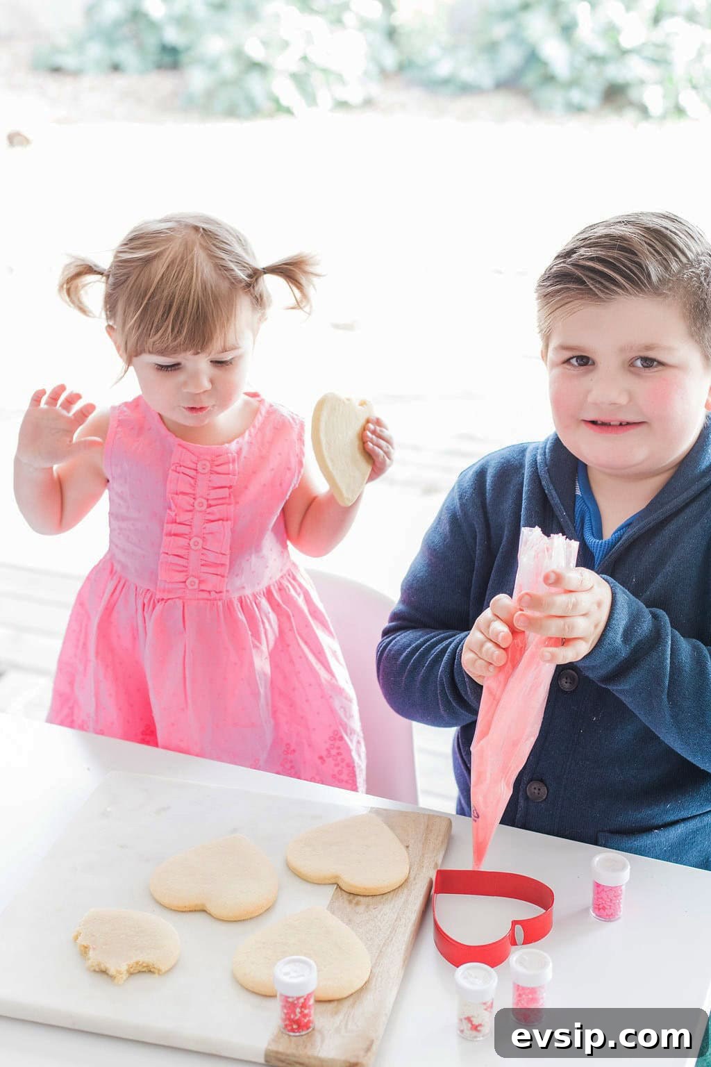 Two small children a girl, and a boy decorating heart shaped cookies. 
