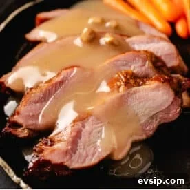 Smoky Turkey Gravy Recipe for Thanksgiving & Leftovers 3 Slices of turkey breasts topped with smoked gravy on a plate with baby carrots.