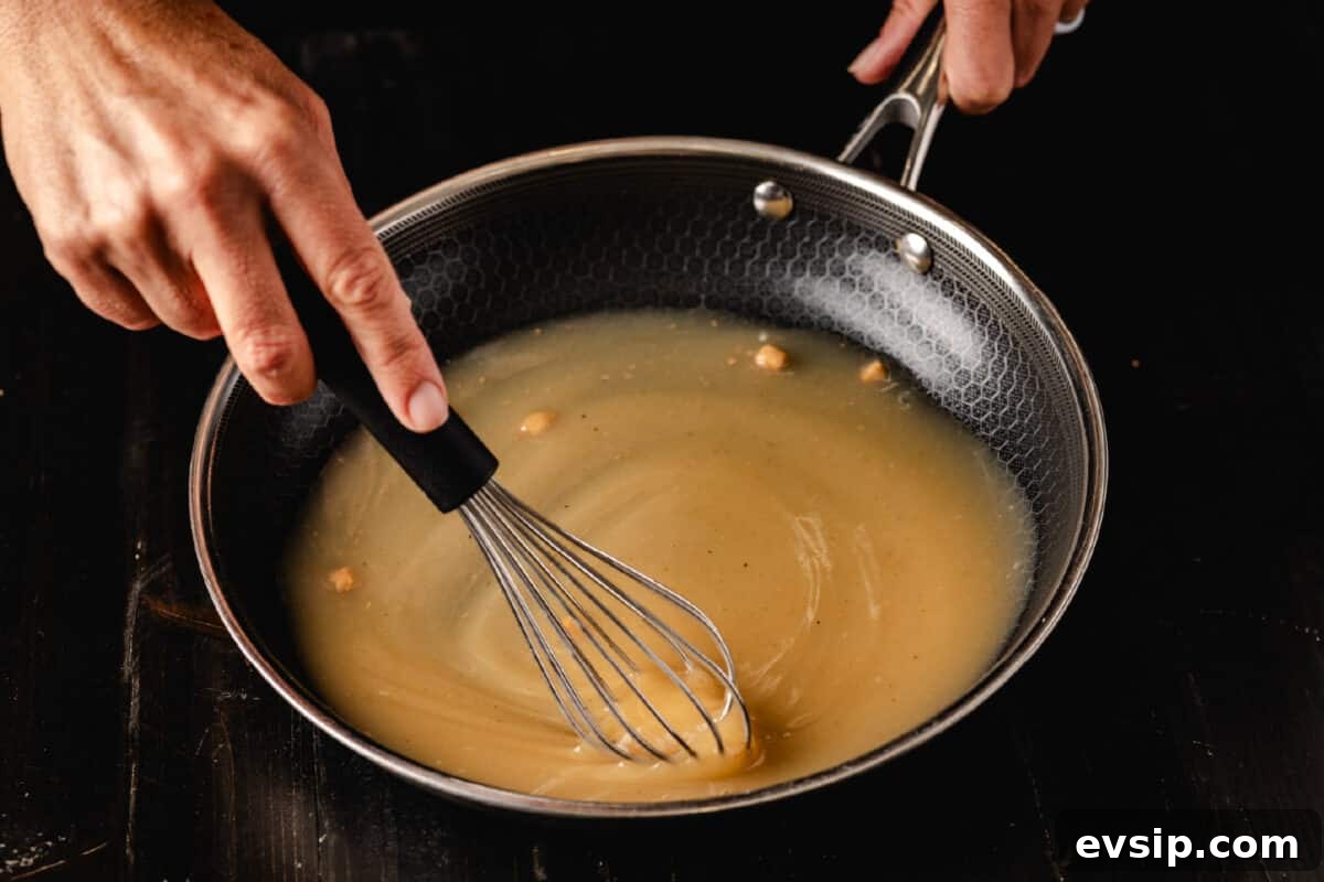 How to Make Gravy from Smoked Turkey A chef's hand whisking a brown liquid in a shallow pan.
