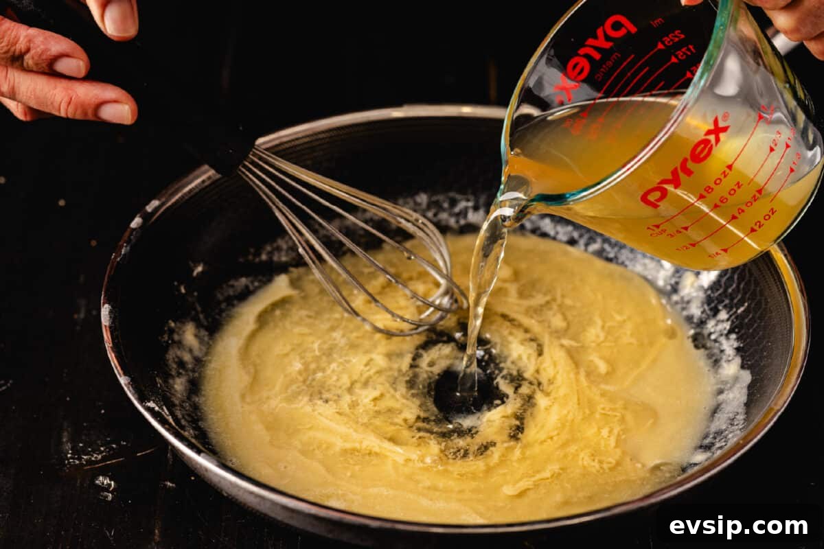 Smoky Turkey Gravy Recipe for Thanksgiving & Leftovers 2 A whisk mixing liquid being poured from a glass measuring cup into a turkey gravy mixture in a pan.