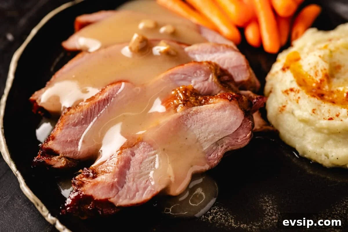 Smoked Turkey Gravy Recipe A sliced turkey breast topped with smoked gravy on a plate with baby carrots and a scoop of mashed potatoes.