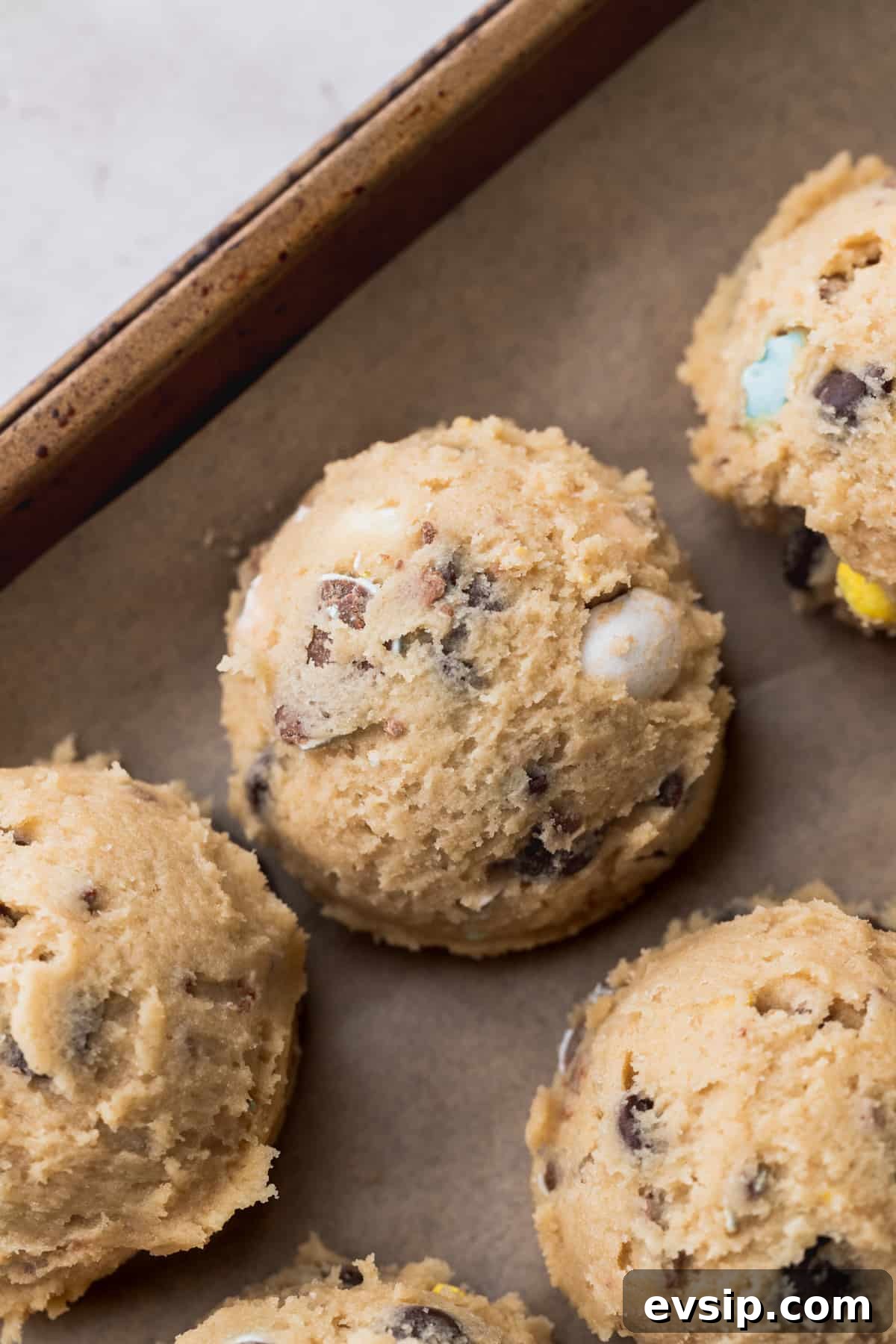 Bite-Sized Mini Egg Cookies with Chocolate Candy Centers 7 Cookie dough balls on a cookie sheet.