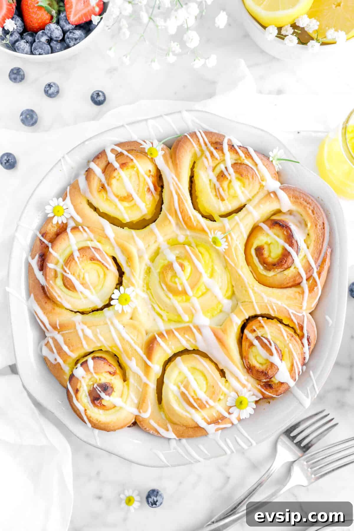 close up overhead shot of lemon rolls with blueberries, flowers, and forks